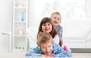 Tres niños felices juegan juntos en la sala, reflejando un ambiente seguro para proteger a tus hijos.