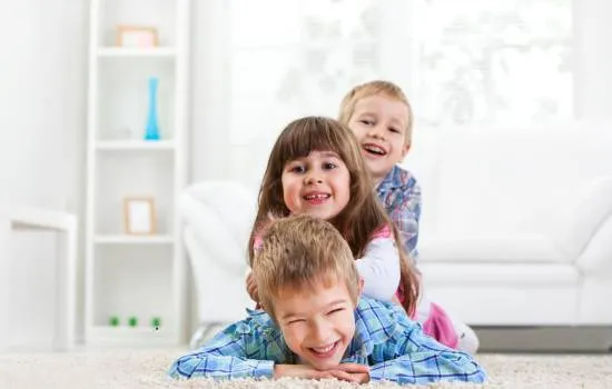Tres niños felices juegan juntos en la sala, reflejando un ambiente seguro para proteger a tus hijos.