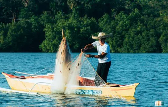 Pescador en un bote lanzando su red en un río, ideal para mostrar cómo se complementa con un sonar para peces en la pesca artesanal.