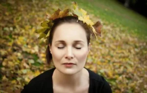 Mujer con los ojos cerrados, rodeada de hojas otoñales, en un momento de conexión interior que simboliza el deseo de reconectar con su energía vital.