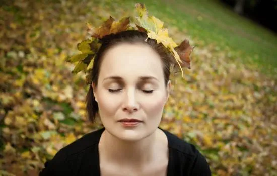 Mujer con los ojos cerrados, rodeada de hojas otoñales, en un momento de conexión interior que simboliza el deseo de reconectar con su energía vital.