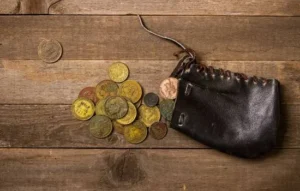 Monedas antiguas saliendo de una bolsita de cuero sobre una mesa de madera, destacando una posible simple moneda.