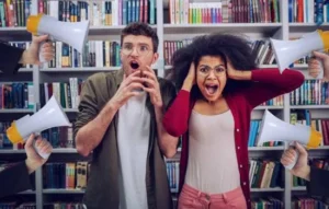 Pareja joven en una biblioteca tapándose los oídos por el ruido de varios megáfonos, simbolizando la necesidad de mejorar tu volumen.