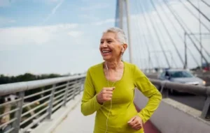 Mujer mayor corriendo al aire libre con auriculares, mostrando cómo mantenerse activa y ponerse en forma con alegría