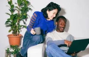 Pareja sonriente mirando una laptop, simbolizando el momento de recuperar tus fotos y revivir recuerdos compartidos.