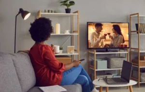 Mujer viendo películas asiáticas en la televisión desde la comodidad de su sofá, con ambiente acogedor y cálido en casa.