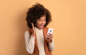 Joven sonriente con el cabello rizado usando un celular blanco, representando la alegría de tener un celular más rápido.